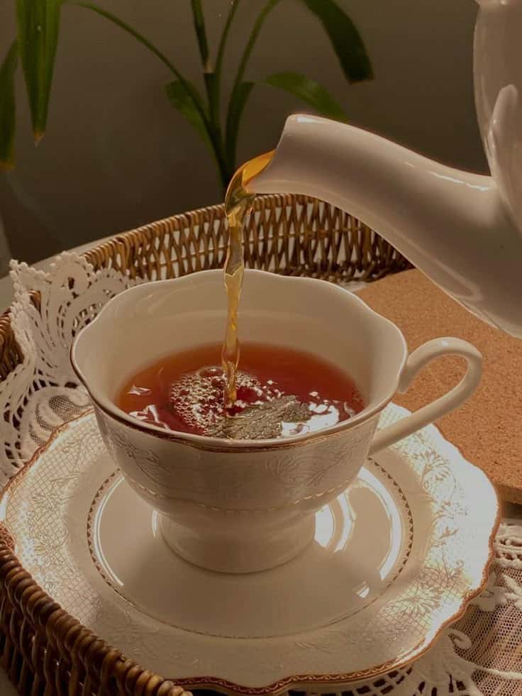 Pouring tea into an elegant teacup on a wicker tray with a cozy atmosphere.