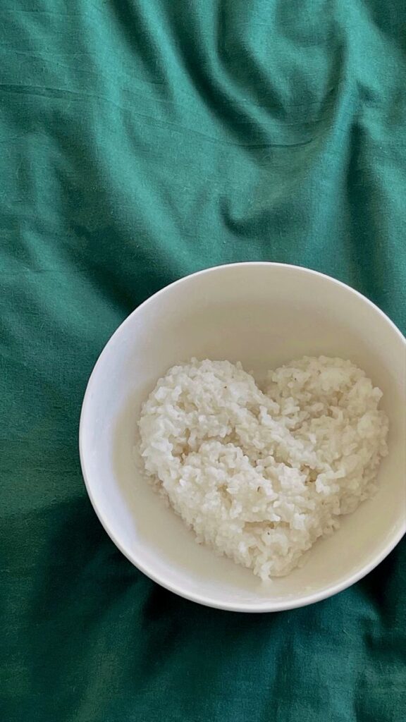 Heart-shaped rice in a white bowl on a green cloth background.