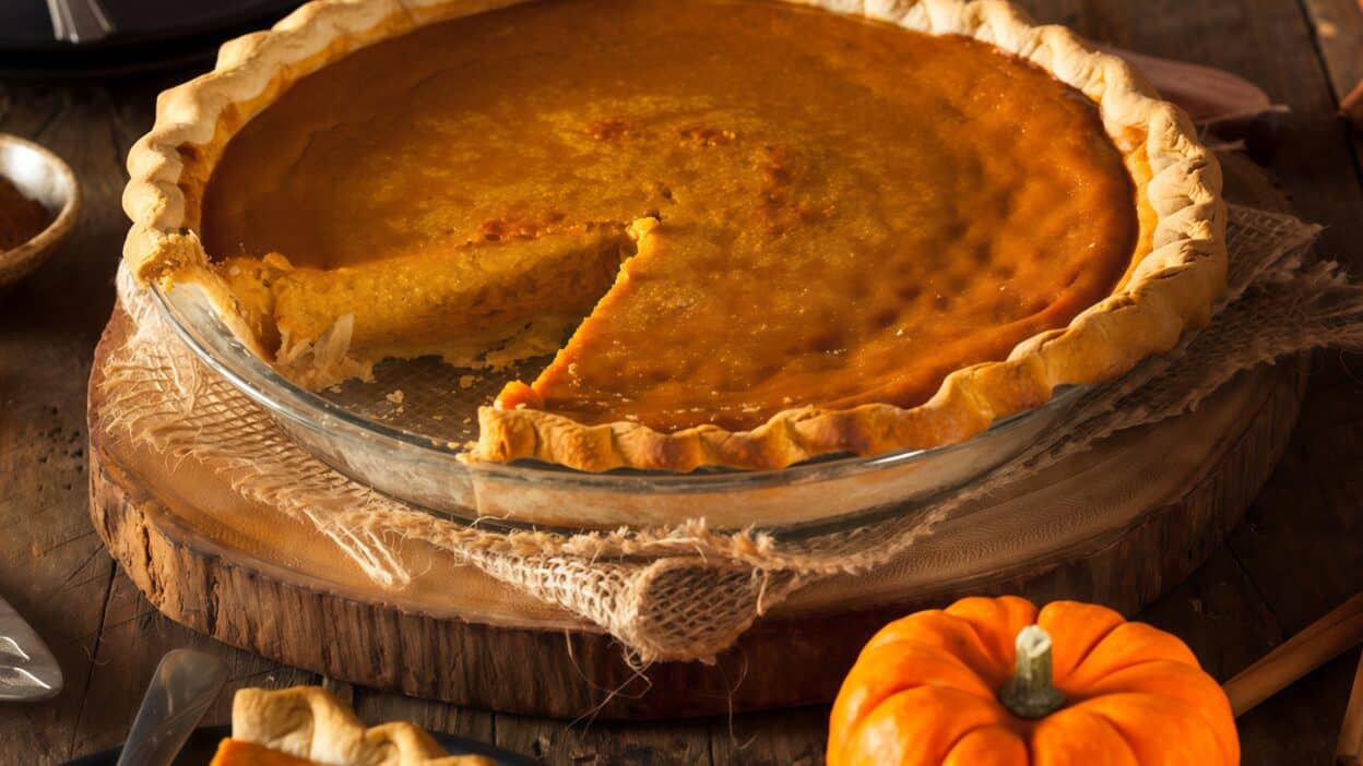 Airbrush-Image-Enhancer-1755979691424 - Cozy Fall Bakes: Easy Recipes for Snacks, Cakes, and Pies | Homemade pumpkin pie with a slice missing, surrounded by spices on a rustic wooden table.