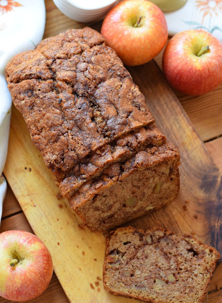 Homemade apple bread loaf with sliced pieces on a wooden board, surrounded by fresh apples.