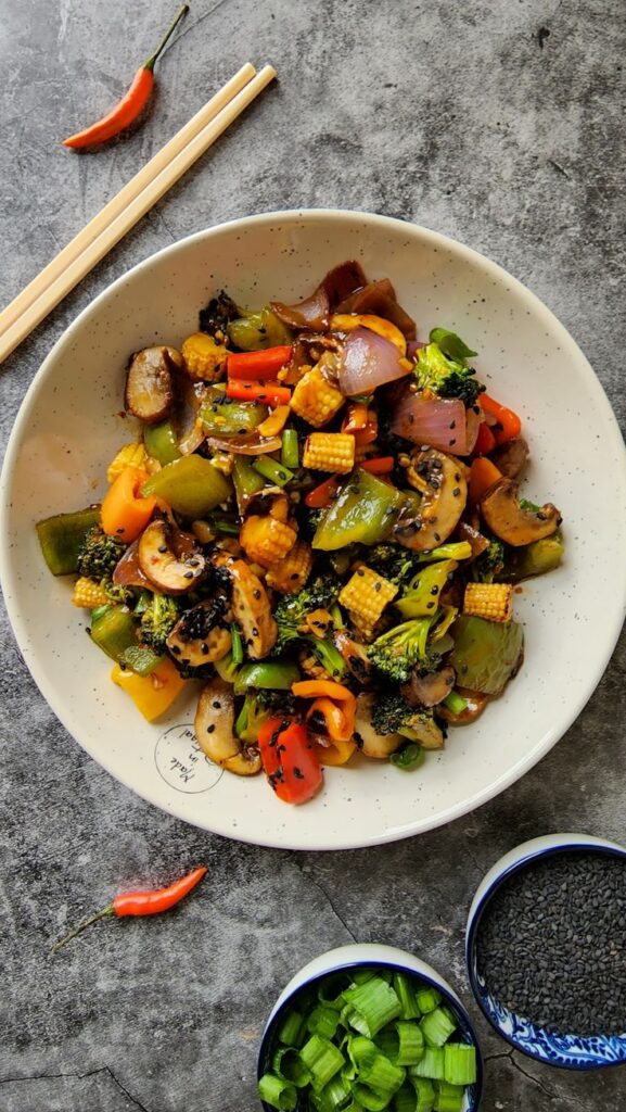 Colorful stir-fried vegetables with mushrooms, baby corn, and broccoli on a plate, garnished with sesame seeds.
