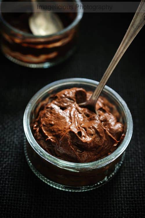 Rich chocolate mousse in a glass jar with a spoon on a dark textured background, perfect dessert indulgence.