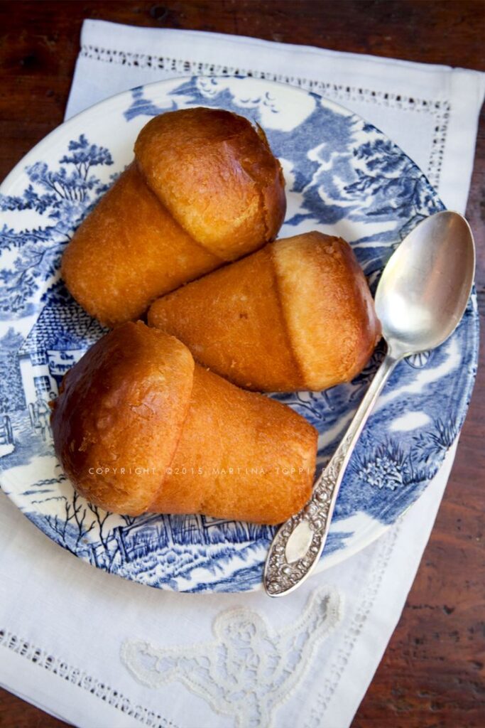Plate of golden babà pastries with a vintage spoon on a decorative blue and white plate.