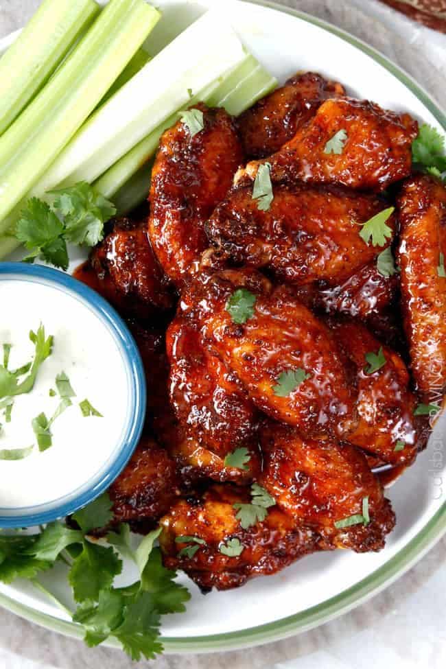 Spicy buffalo chicken wings with cilantro, celery sticks, and creamy ranch dip on a white plate.