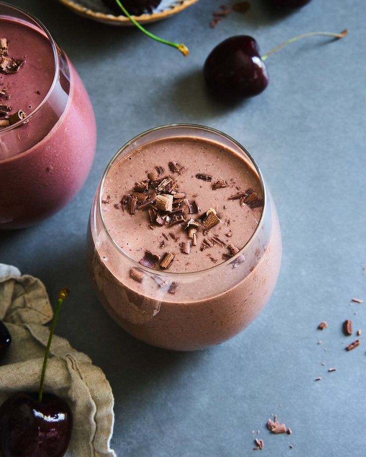 Chocolate cherry smoothie topped with chocolate shavings in a glass on a gray table with fresh cherries nearby.