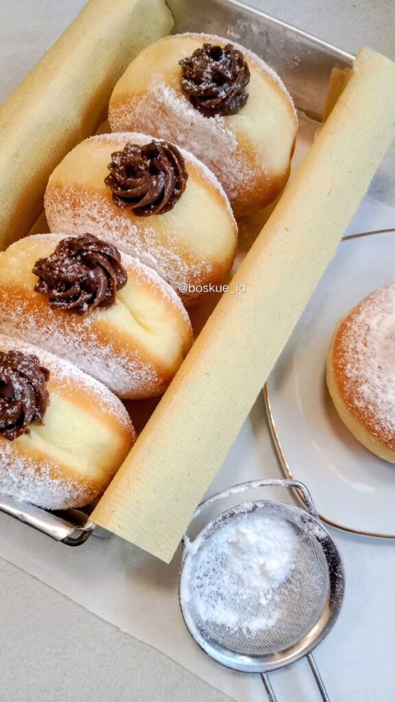Fluffy doughnuts with chocolate filling and powdered sugar in a tray, ideal for desserts or breakfast treats.