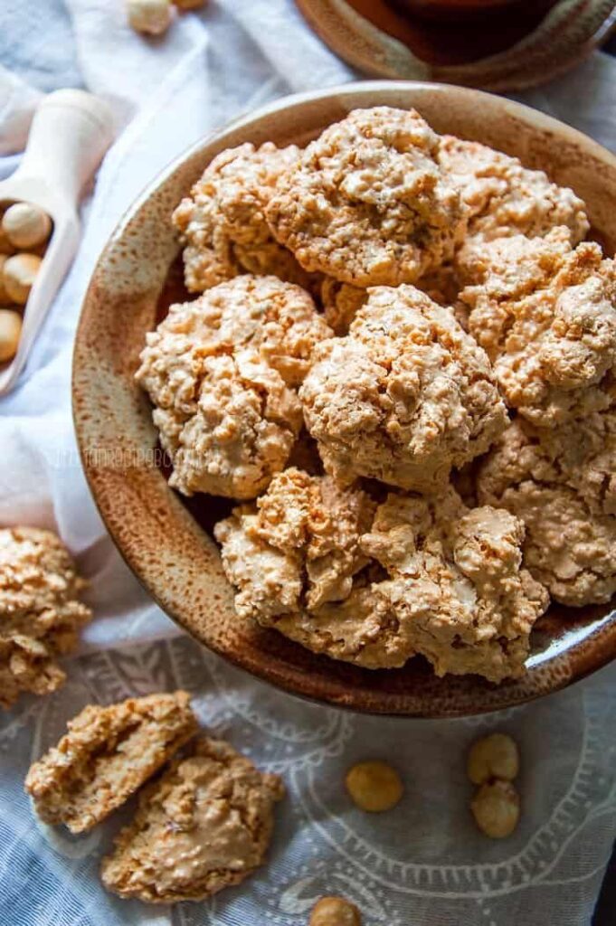 Rustic almond cookies in a ceramic bowl, surrounded by whole almonds on a textured cloth.