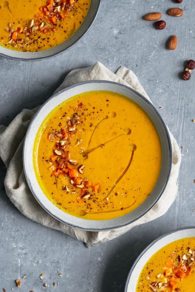 Creamy carrot soup garnished with nuts and pepper, served in a bowl on a gray background.