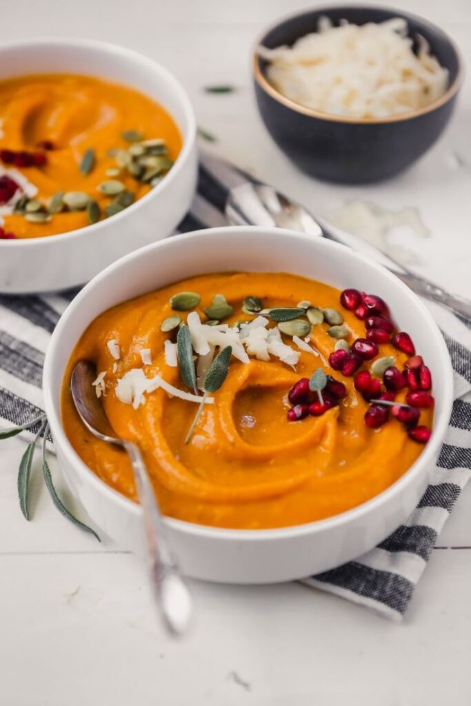 Creamy pumpkin soup topped with seeds, cheese, and pomegranate in a bowl, perfect for autumn meals.