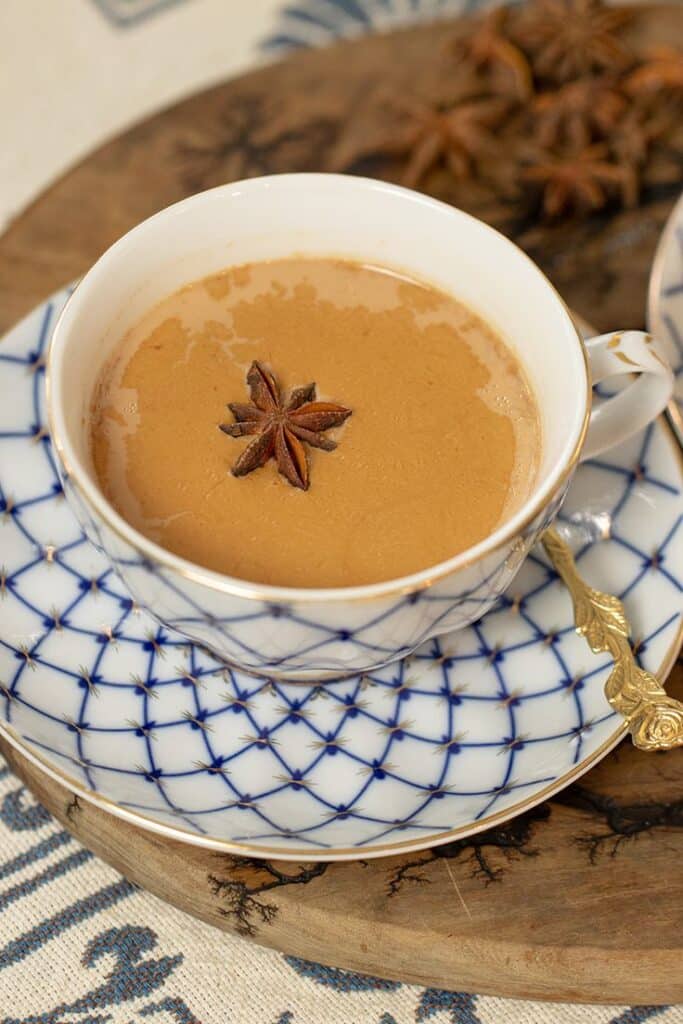 Creamy chai tea with star anise in an elegant cup and saucer, placed on a wooden tray.