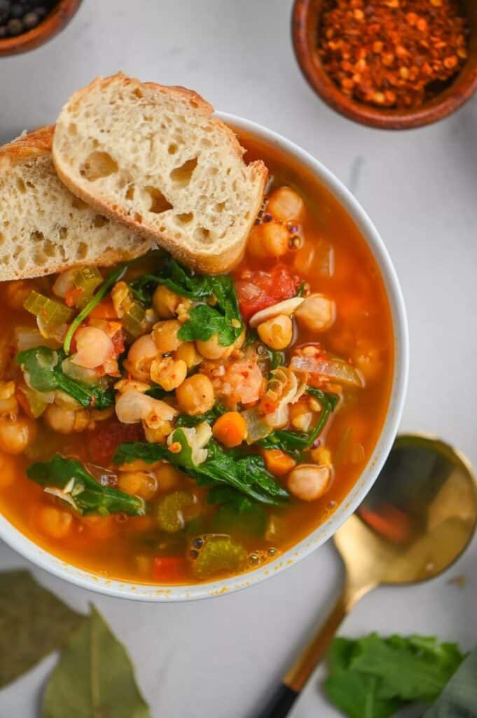 Chickpea vegetable soup with spinach and bread, garnished with spices. Perfect for a healthy, hearty meal.