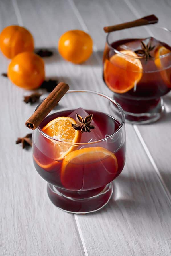 Mulled wine in glasses with orange slices, cinnamon sticks, and star anise on a wooden table.