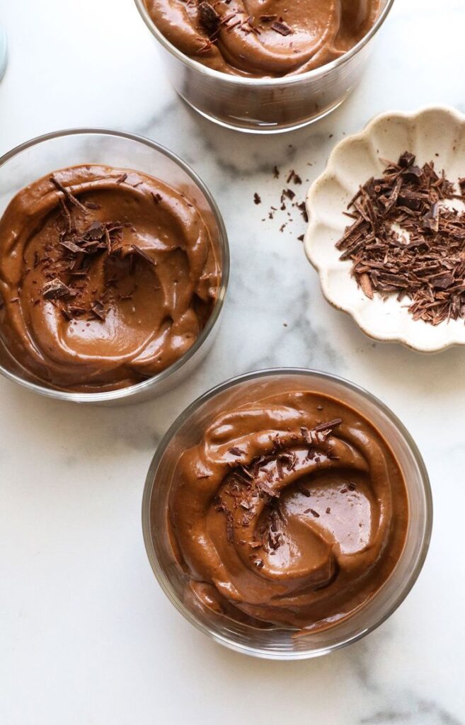 Creamy chocolate pudding in glass bowls topped with chocolate shavings on a marble surface.