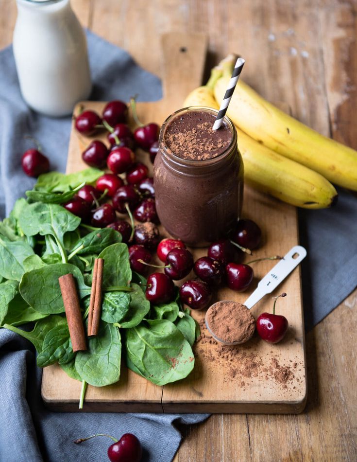 Chocolate smoothie with cherries, bananas, spinach, and cinnamon on a wooden board, ideal for a healthy breakfast.
