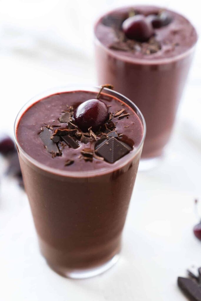 Rich chocolate smoothie topped with cherries and chocolate shavings in a glass.