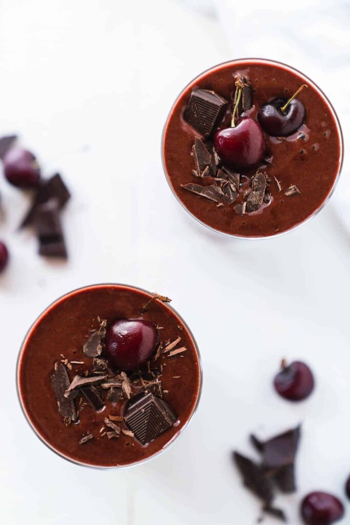 Two glasses of chocolate mousse topped with cherries and chocolate shavings on a white background.