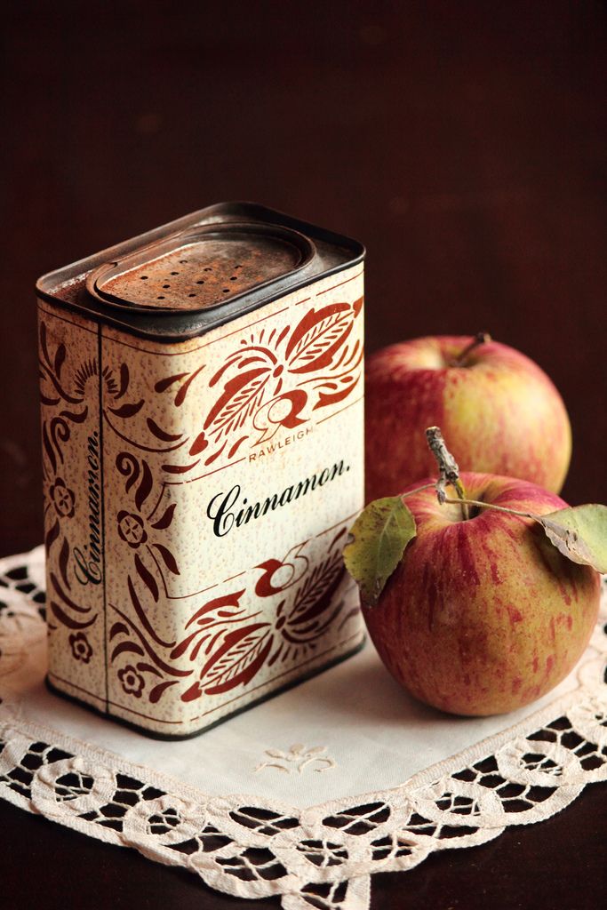 Vintage cinnamon tin with apples on lace cloth; rustic kitchen decor.