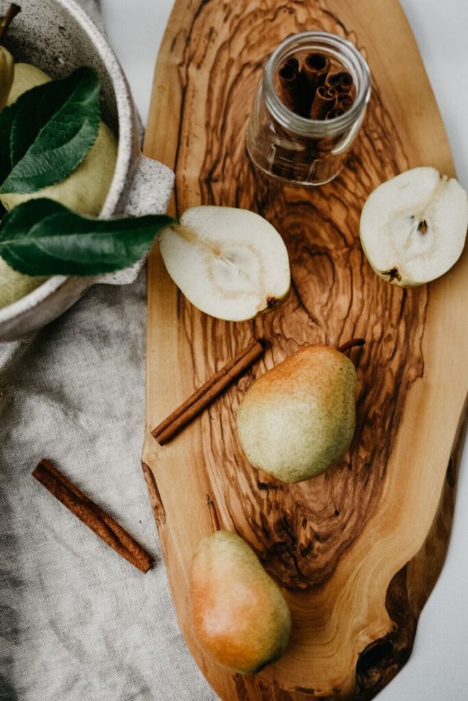 Fresh pears and cinnamon sticks on a wooden board, perfect for autumn recipes and cozy kitchen vibes.
