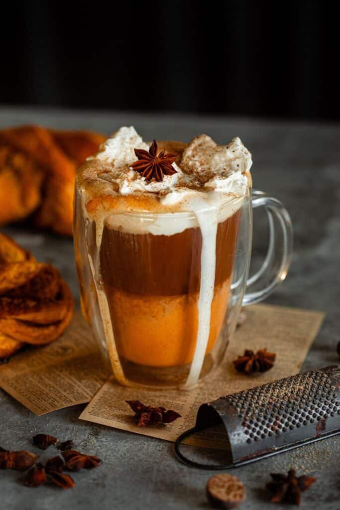 Spiced pumpkin latte with whipped cream in glass mug, garnished with star anise, on rustic table setting.
