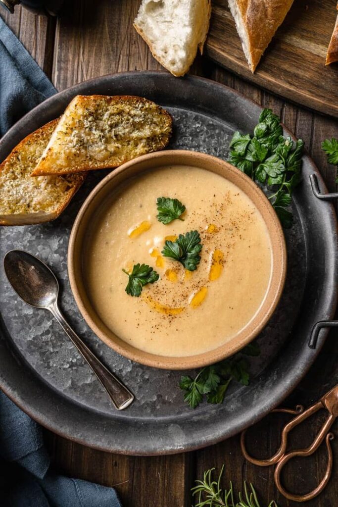 Creamy soup garnished with parsley and served with toasted bread on a rustic tray.