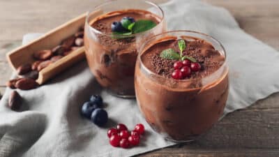 Two glasses of rich chocolate mousse topped with fresh berries and mint leaves on a wooden table.