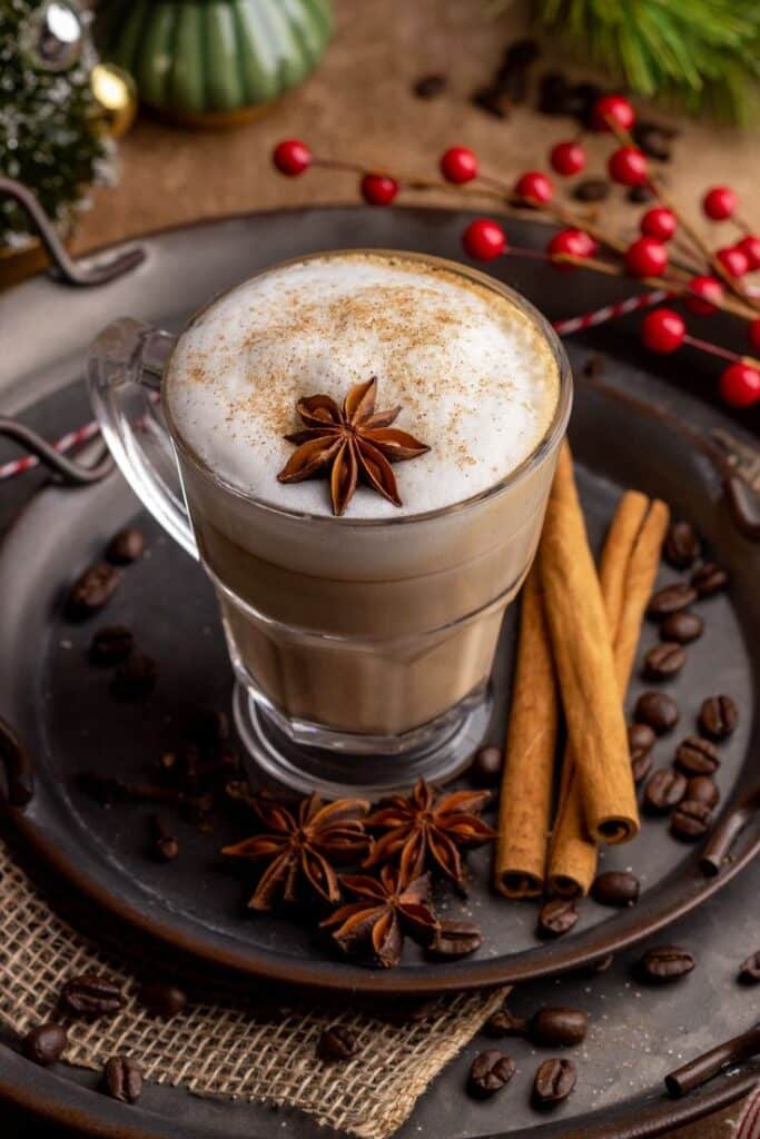 Creamy spiced latte with star anise, surrounded by cinnamon sticks and coffee beans on a festive table setting.