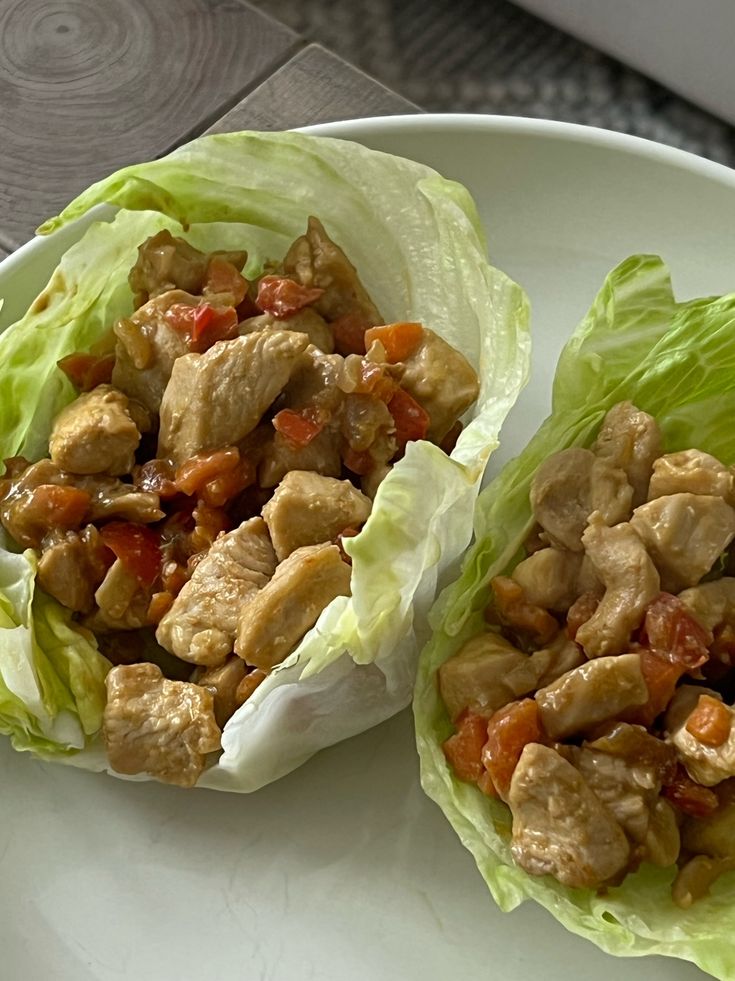 Chicken lettuce wraps with diced vegetables on a white plate, showcasing a healthy, low-carb meal option.