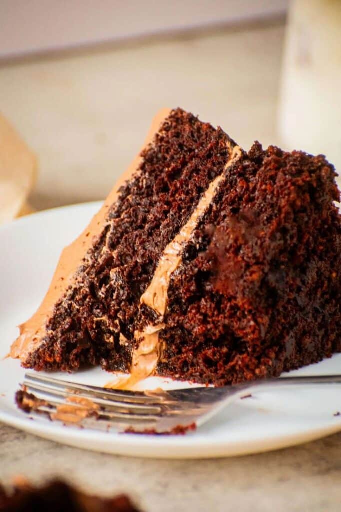 Delicious slice of rich chocolate cake with creamy frosting on a plate, ready to enjoy with a fork.