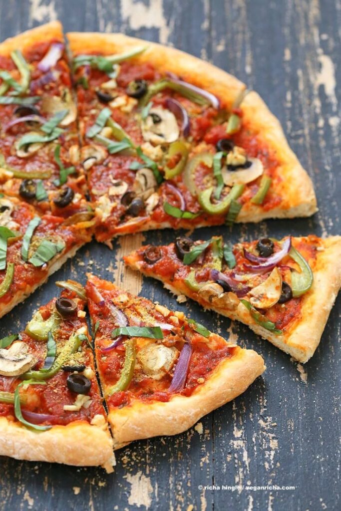 Easy Veggie Vegan Pizza with 20 minute Crust - Vegan Richa - Master the Art of Homemade Pizza with Fun, Simple Steps | Delicious vegan pizza with olives, mushrooms, peppers, and fresh basil on a rustic wooden table background.