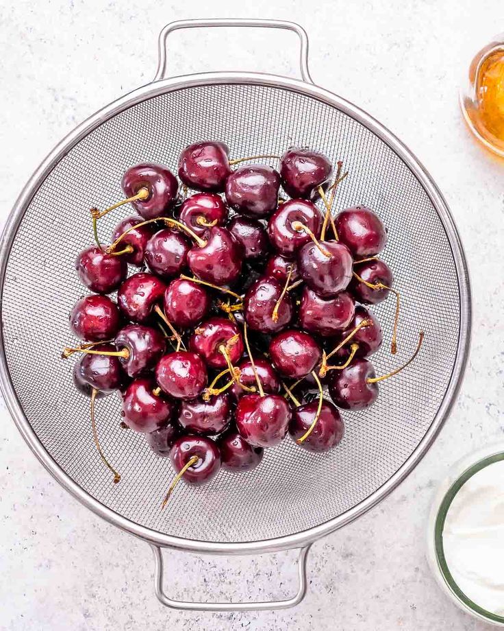 Fresh cherries in a metal strainer on a light countertop, ready for use in recipes or as a healthy snack.