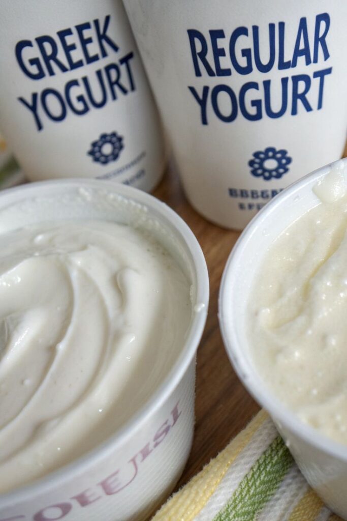 Containers of Greek and regular yogurt on a table showcasing creamy textures.