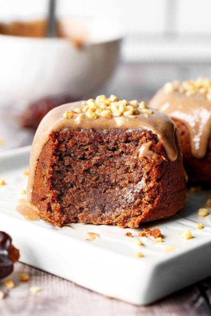 Delicious sticky toffee pudding with caramel glaze and chopped nuts on a white plate, perfect dessert treat.