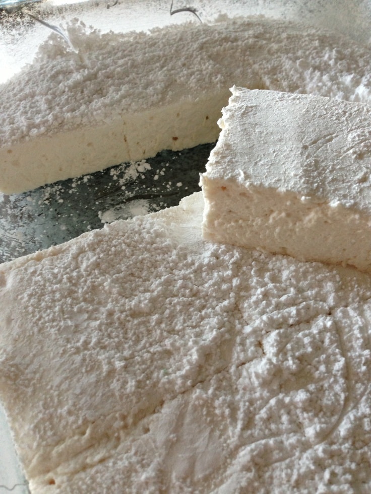 Close-up of soft, fluffy marshmallow squares dusted with confectioners' sugar in a glass dish.
