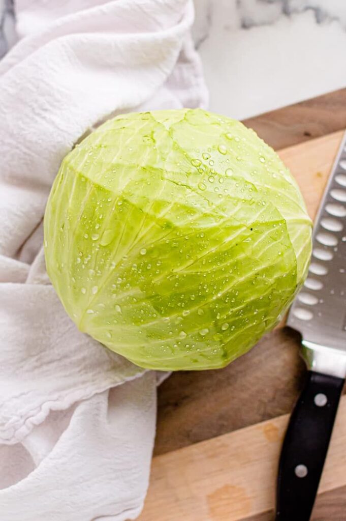Fresh green cabbage on a kitchen counter with knife and cloth, ready for cooking preparation.