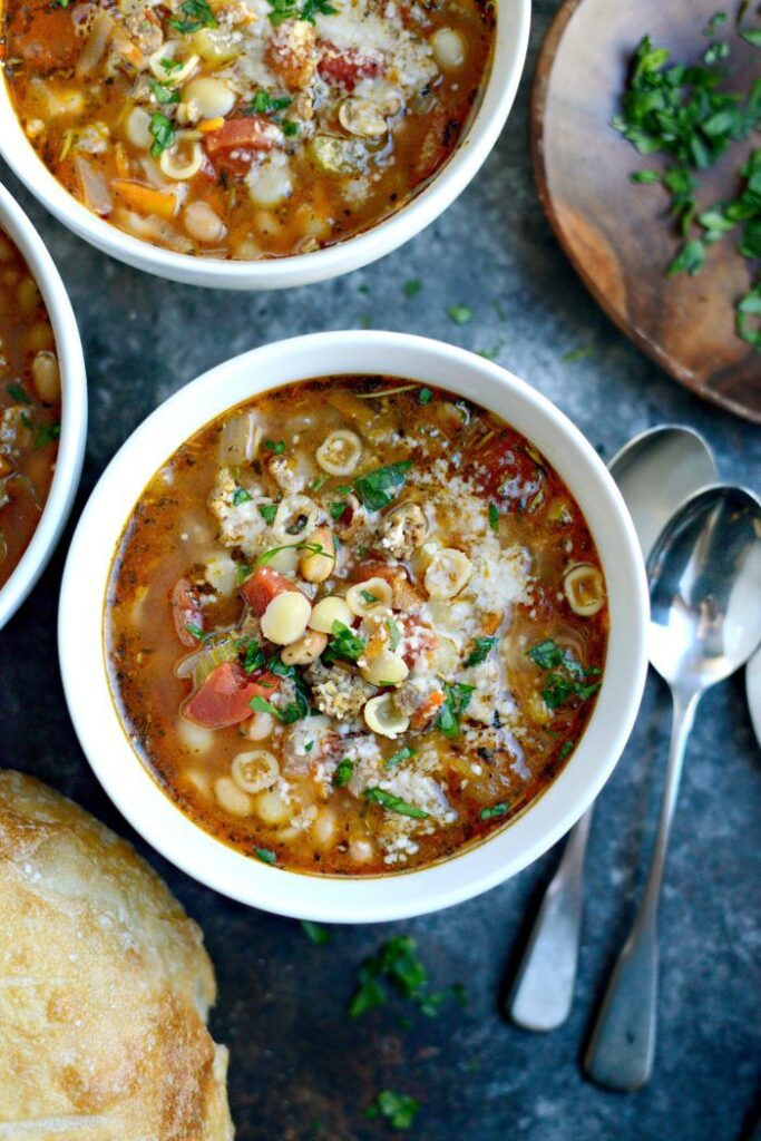 Hearty vegetable soup in a white bowl with pasta and beans, garnished with fresh herbs.