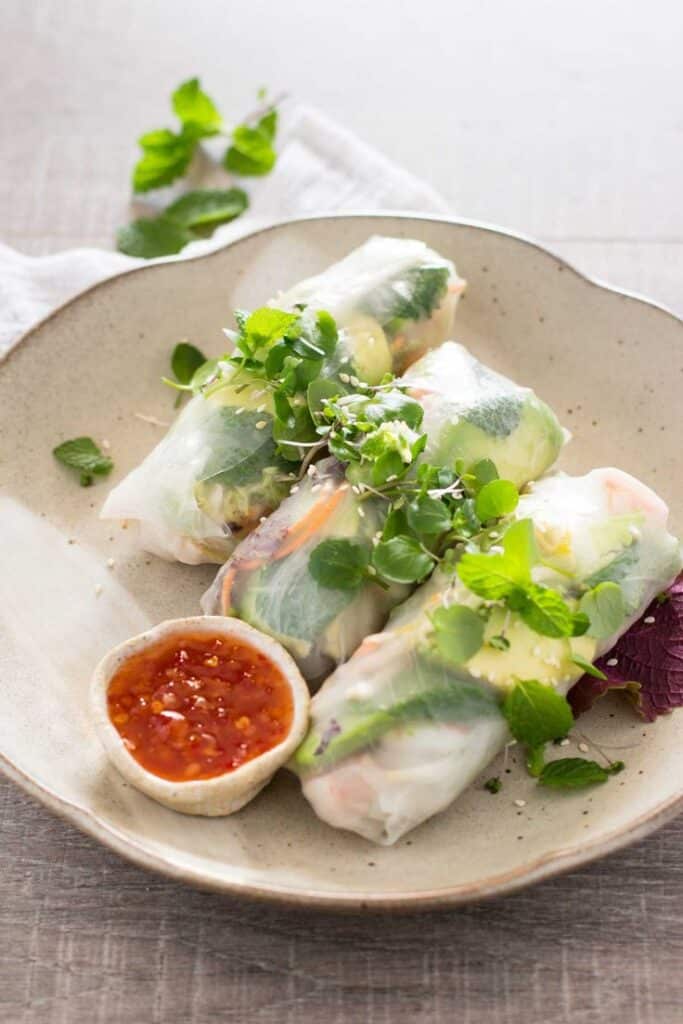 Fresh Vietnamese spring rolls with herbs and dipping sauce on a plate.