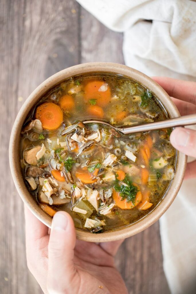 Bowl of wild rice and vegetable soup with carrots, mushrooms, and spinach on a rustic wooden table.