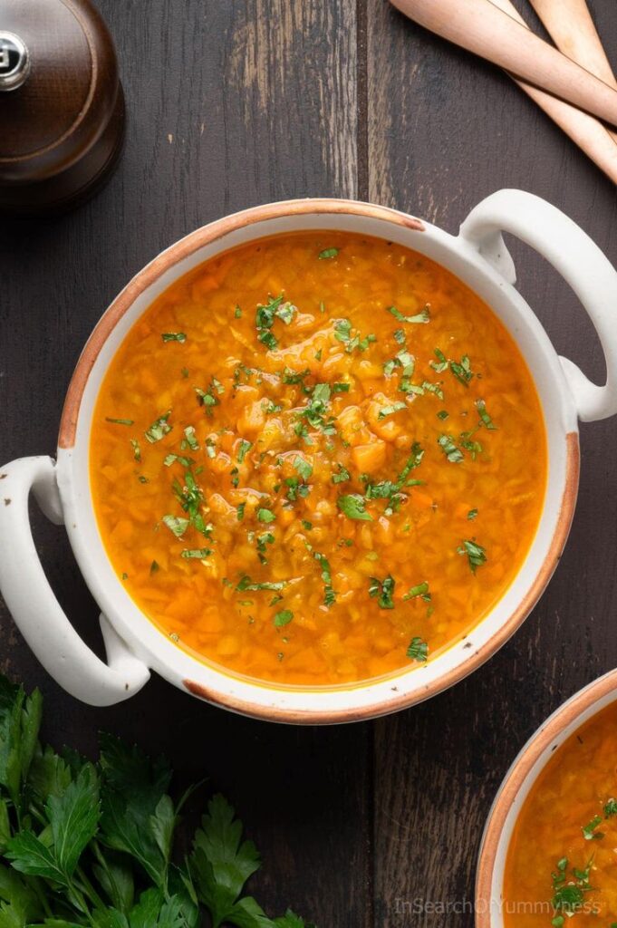 Hearty orange soup garnished with fresh herbs in a ceramic bowl on wooden table. Perfect for a cozy meal.