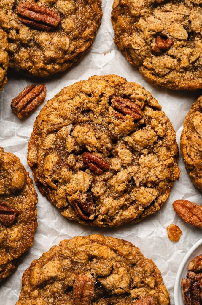 Close-up of delicious homemade oatmeal cookies topped with pecans, on a parchment-lined baking sheet.