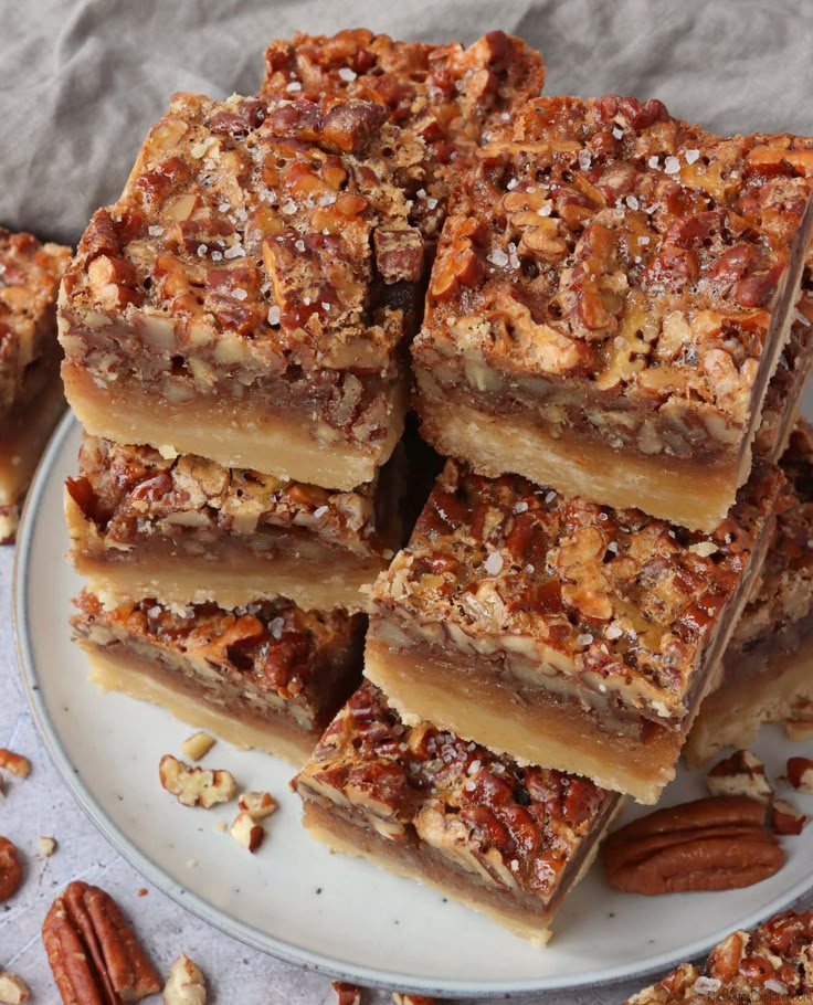 Close-up of stacked pecan pie bars with a flaky crust and caramelized nut topping on a white plate.