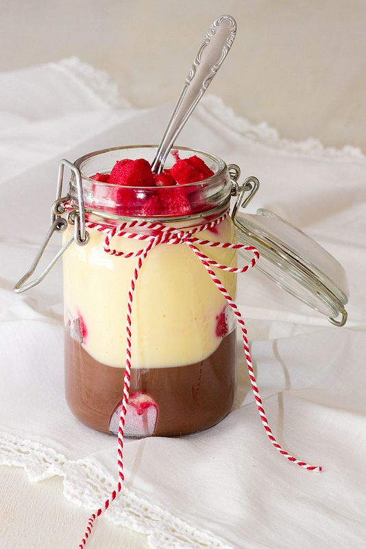 Layered dessert jar with chocolate, vanilla pudding, and raspberries, topped with red fruit and a decorative string.