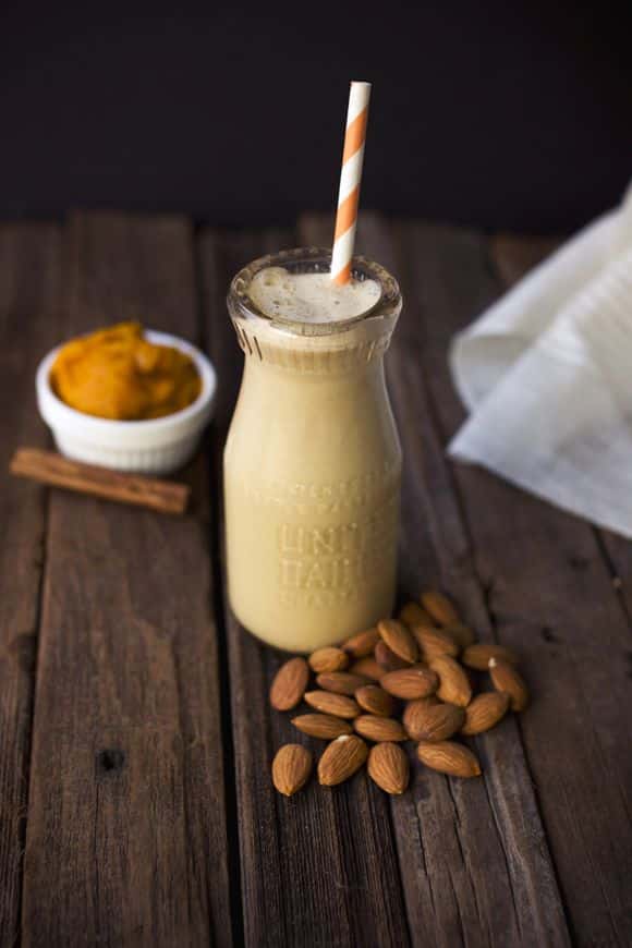 Creamy pumpkin almond smoothie in a glass bottle with straw on wooden table. Healthy fall drink with almonds and cinnamon.