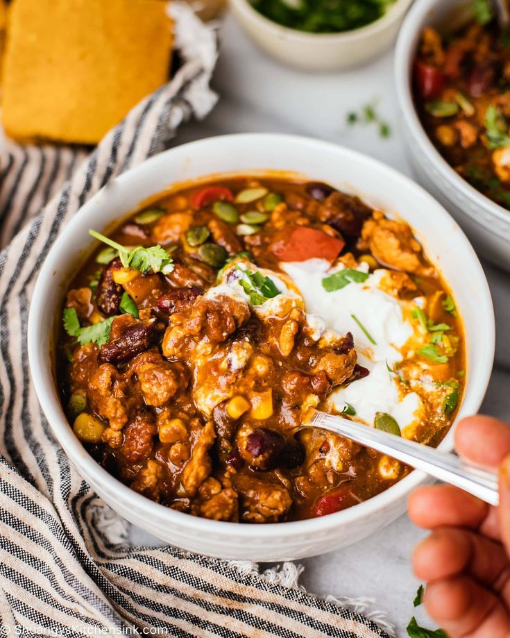 Hearty beef and bean chili in a white bowl with sour cream and fresh cilantro, perfect for comfort food lovers.