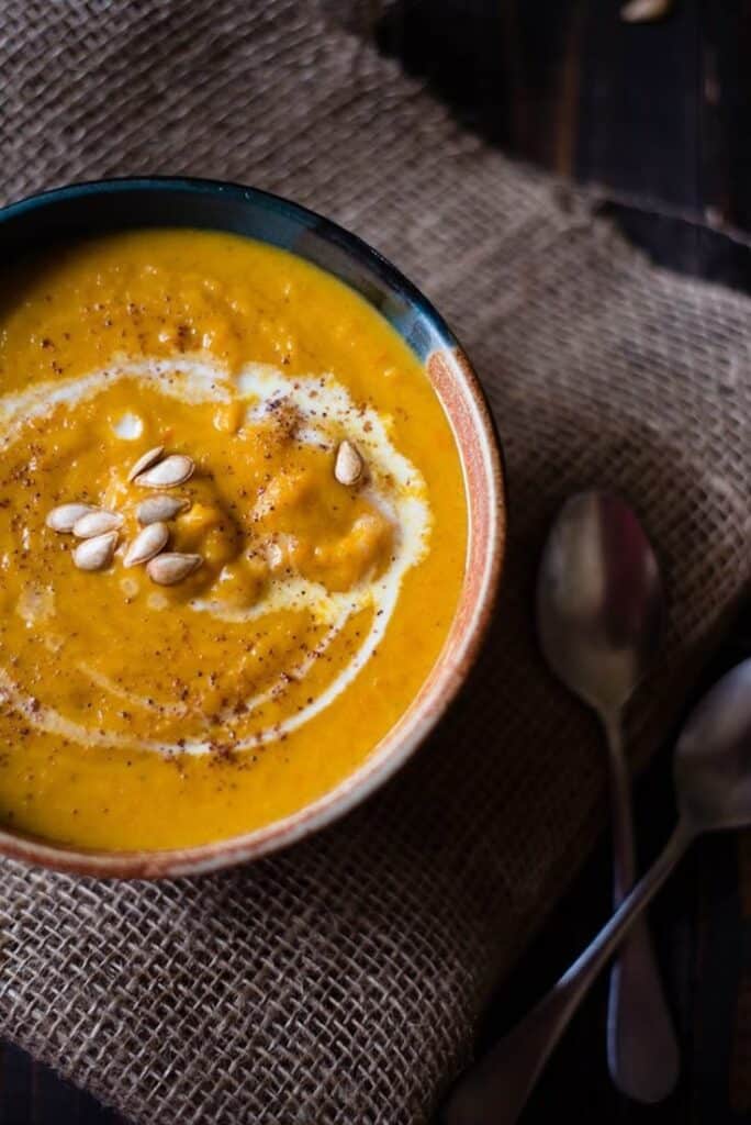 Creamy pumpkin soup in bowl garnished with cream and seeds on a rustic backdrop.