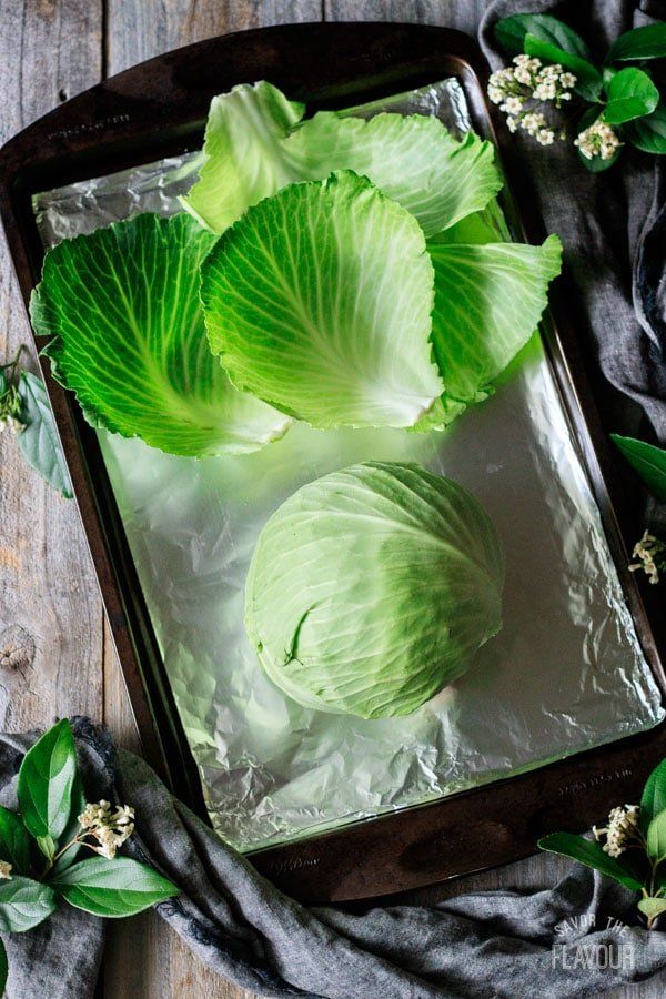 Fresh cabbage leaves and whole cabbage on a foil-lined baking tray, surrounded by rustic decor.