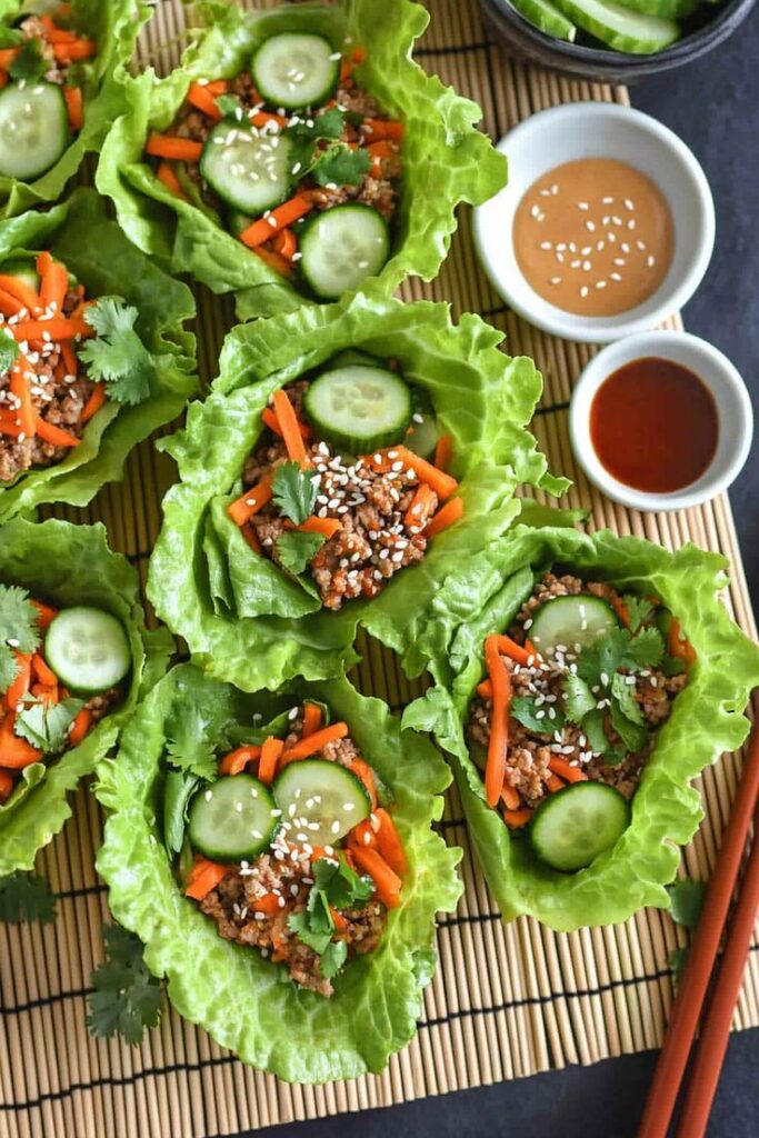 Fresh lettuce wraps with ground meat, cucumbers, carrots, and sesame seeds, served with dipping sauces.