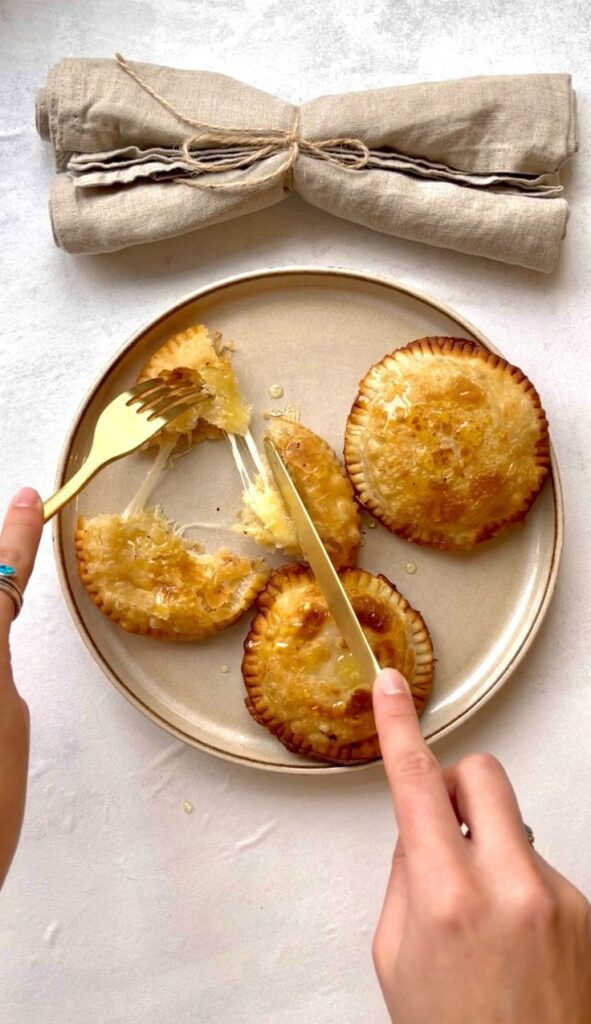 Golden fried hand pies being cut open on a plate, with gooey melted cheese oozing out.