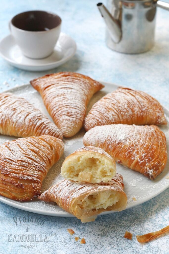 Delicious Italian sfogliatelle pastries with powdered sugar on a plate beside a cup of coffee and a metal pot.