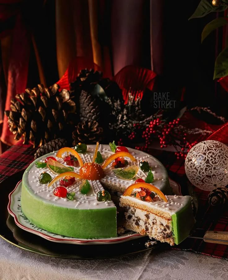 Festive cake with colorful fruit toppings and green icing, perfect for Christmas celebrations. Pinecones and decor in background.