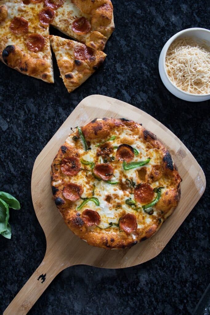 Sourdough Pizza Crust - Kitchen Joy - Master the Art of Homemade Pizza with Fun, Simple Steps | Delicious homemade pepperoni pizza on a wooden paddle with grated cheese on the side.